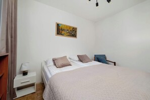 A bedroom with a bed, a nightstand, a chair, a painting, and a lamp.