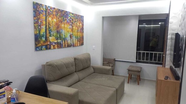 A living room with a beige sofa, a painting on the wall, a small table, and a TV on a stand. - Complete apartment no turu 5 kms praias aracagy (São José de Ribamar)