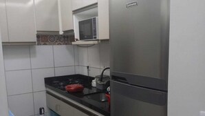 A compact kitchen with white cabinets, a stainless steel refrigerator, a microwave, and a gas stove. - Complete apartment no turu 5 kms praias aracagy (São José de Ribamar)