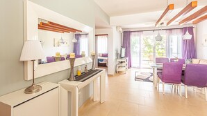 Un espace repas moderne avec une console blanche, des chaises violettes et une grande fenêtre agrémentée de rideaux.