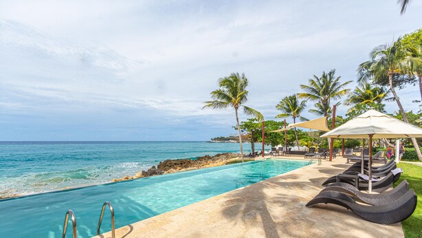 Un espace aménagé au bord de la piscine, avec des chaises longues et des parasols, offrant une vue sur l’océan.