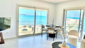 A spacious living room with a balcony overlooking the sea, a dining area with a table set for four, and a TV mounted on the wall. - L'onde Turquoise - Waterfront apartment (Carthage)