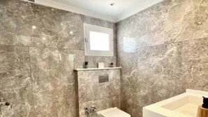 A modern bathroom with a marble wall, a built-in toilet, a shower, and a vanity with a sink. - L'onde Turquoise - Waterfront apartment (Carthage)