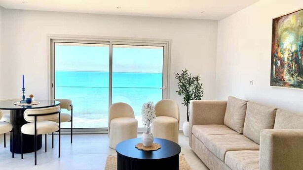 A modern living room with a round coffee table, beige sofa, and a dining area with chairs. - L'onde Turquoise - Waterfront apartment (Carthage)