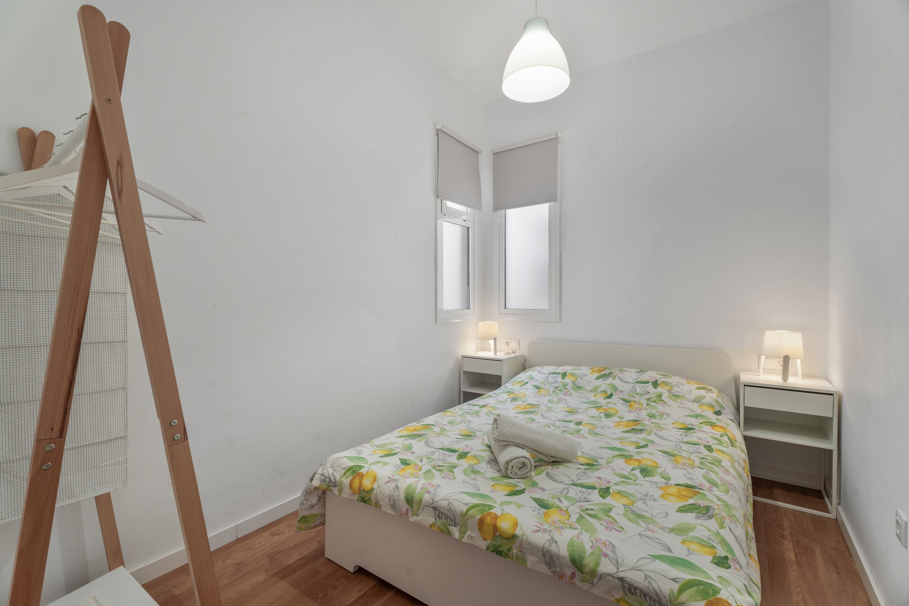 Une chambre à coucher comprenant un lit, un chevalet en bois, un miroir, des tables de chevet et un luminaire suspendu.