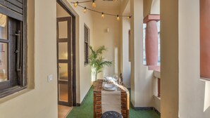 A narrow hallway with a wooden table set for dining, a potted plant, and string lights.