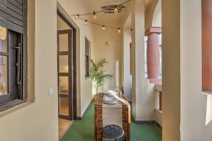 Un couloir étroit avec une table en bois dressée pour le repas, une plante en pot et des guirlandes lumineuses.
