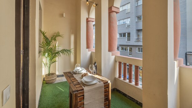 A balcony with a table set for dining, a potted plant, and a view of a building.
