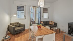 A modern living room with a wooden dining table, a grey sofa, a grey armchair, and a TV on a stand.