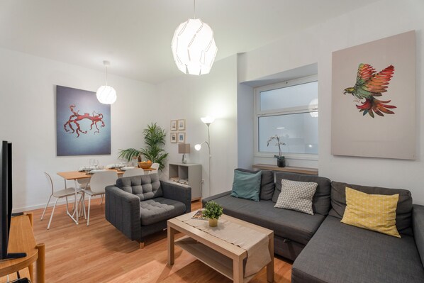 A modern living room with a sofa, armchair, coffee table, and a dining area with a table and chairs.