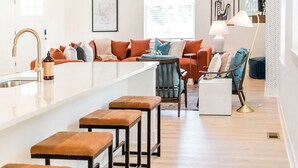 A modern kitchen with a central island, a dining area with bar stools, and a seating area with a sofa and chairs.
