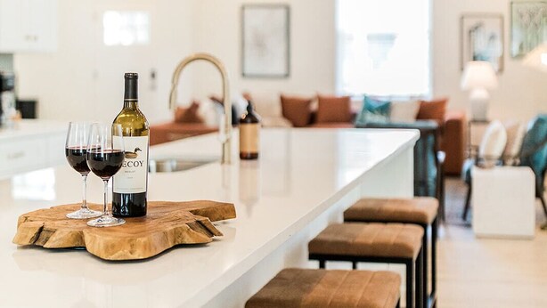 A modern kitchen with a long island, bar stools, and a wine bottle.