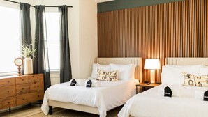 A hotel room with two beds, a wooden dresser, a mirror, and a lamp.