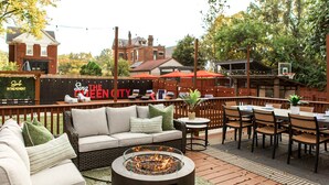 An outdoor patio area with a fire pit, seating, and a view of a restaurant named "The Queen City."