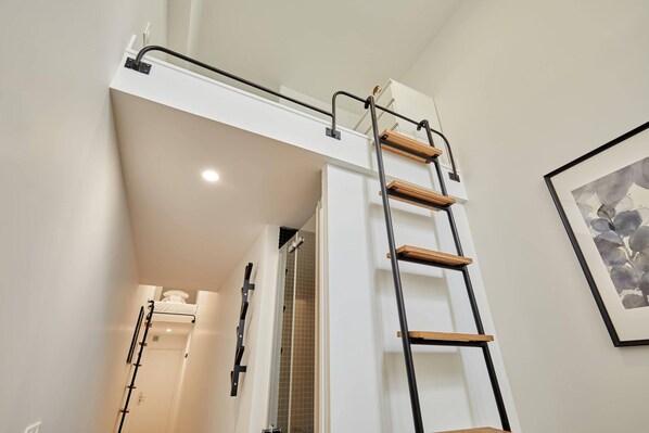 Une salle de bain moderne avec une douche, une porte blanche et un escalier menant à une mezzanine.