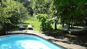 Une piscine entourée d’arbres et de chaises longues, avec une terrasse en bois.