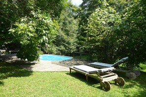 Un jardin avec une terrasse en bois, une piscine et un fauteuil de relaxation.