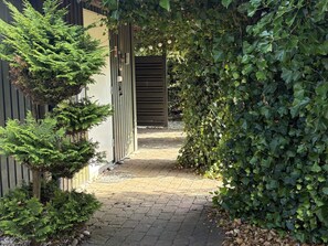 A paved pathway leading to a gated entrance, surrounded by lush greenery and a variety of plants.