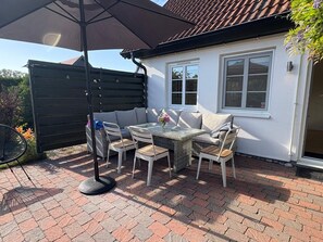An outdoor patio with a table and chairs, a black umbrella, and a white building with windows.