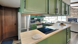 A modern kitchen with green cabinets, a stainless steel refrigerator, a microwave, and a built-in stove. - Fireside Cabin | Close to Midtown + Trails (Ruidoso)