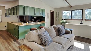 A modern living room with a beige sofa, a wooden coffee table, and a kitchen area with green cabinets. - Fireside Cabin | Close to Midtown + Trails (Ruidoso)
