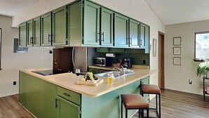 A modern kitchen with green cabinets, a wooden countertop, and a built-in island with bar stools. - Fireside Cabin | Close to Midtown + Trails (Ruidoso)