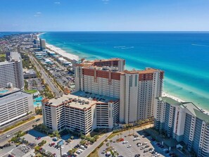 A high-rise hotel with multiple floors, a parking lot, and a beach view.