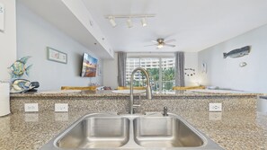 A modern kitchen with granite countertops, a double sink, and a ceiling fan.