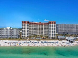 A beachfront hotel with multiple high-rise buildings, a sandy beach, and a clear blue sky. - Emerald Tide Retreat 327-Gulf Views-Sleeps 6 (Panama City Beach)