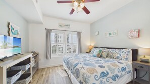A bedroom with a bed, a desk, a television, and a ceiling fan.