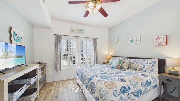 A bedroom with a bed, a desk, a television, and a ceiling fan.