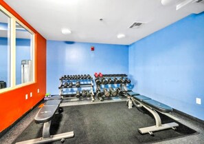 Ein Fitnessstudio mit Krafttrainingsgeräten, einer Bank und auf Hantelständer geordneten Kurzhanteln.