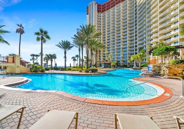 A hotel with a large swimming pool, palm trees, and a high-rise building.