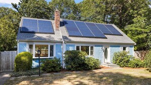Ein Haus mit Solaranlage auf dem Dach, einer Veranda und einem gepflegten Rasen.