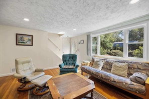 A living room with a sofa, a rocking chair, a coffee table, and a window with a view of trees.