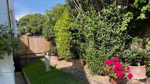 Ein gepflegter Garten mit verschiedenen Pflanzen und Blumen, einem Ziegelweg und einem Holzzaun.