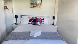 Ein ordentlich bezogenes Bett mit weißer Bettwäsche und zwei Zierkissen, ein gefaltetes Handtuch auf dem Bett sowie ein Bild an der Wand darüber.