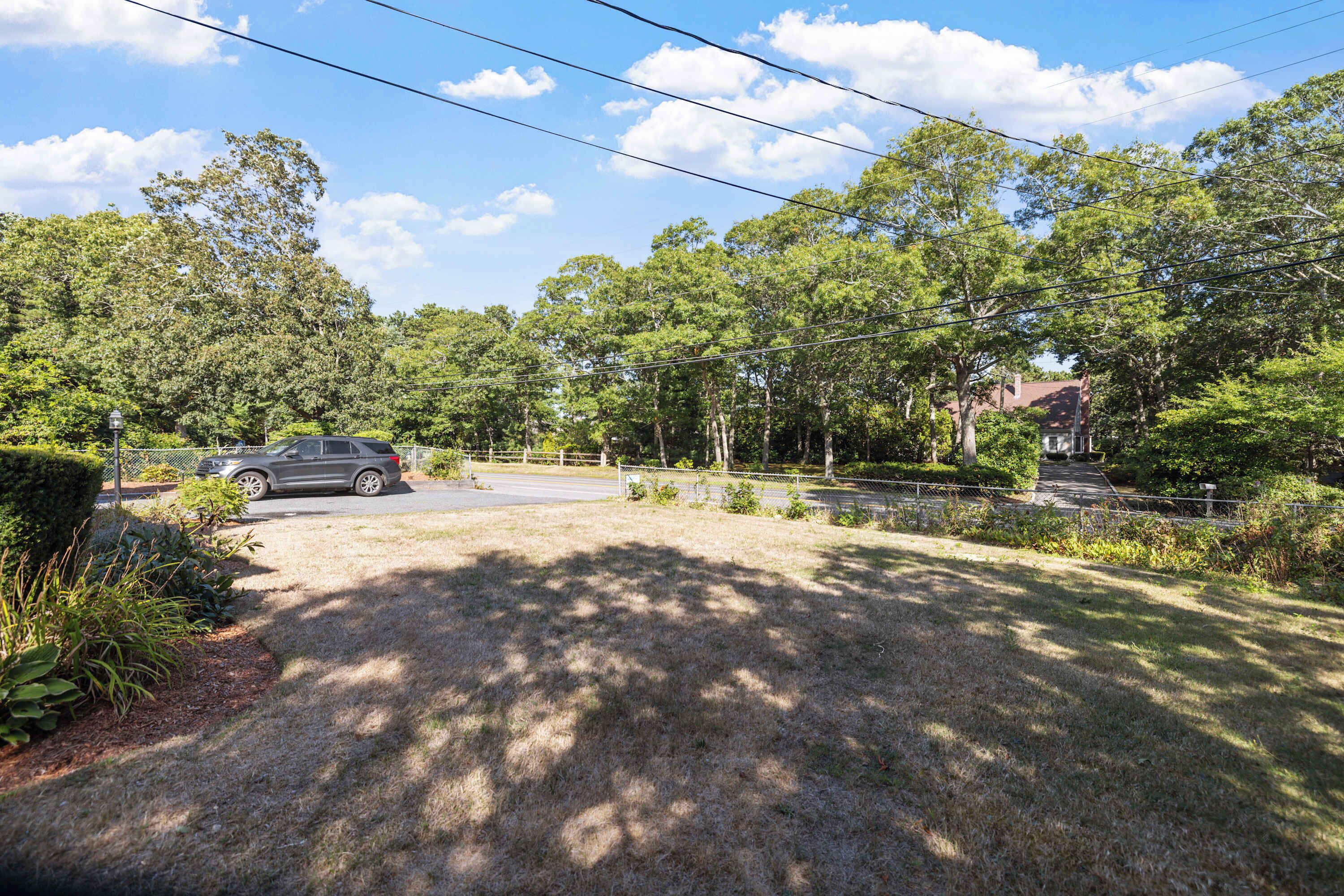A residential area with a paved driveway, a parked car, and a house with a red roof.