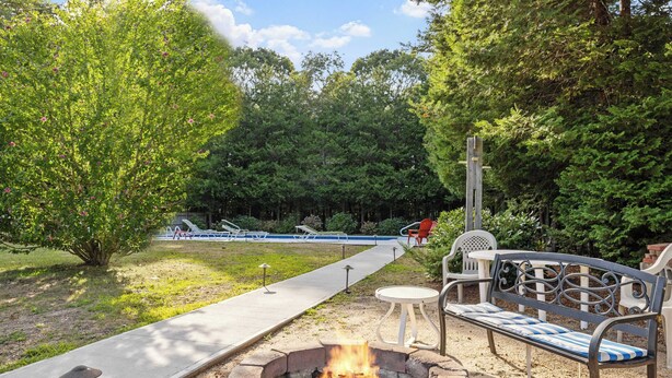 A fire pit with a bench and table, surrounded by a pathway and trees. - Cape Cod Family Escape w/ Pool, Game Room & Patio (Falmouth)