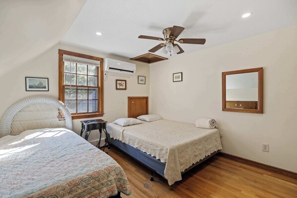 A bedroom with a bed, a chair, a desk, a ceiling fan, and a window.