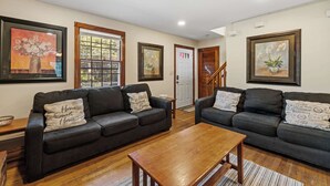A living room with two dark sofas, a wooden coffee table, and framed artwork on the walls. - Cape Cod Family Escape w/ Pool, Game Room & Patio (Falmouth)