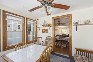Zona pranzo con tavolo e sedie in legno, ventilatore a soffitto e vista sulla cucina.