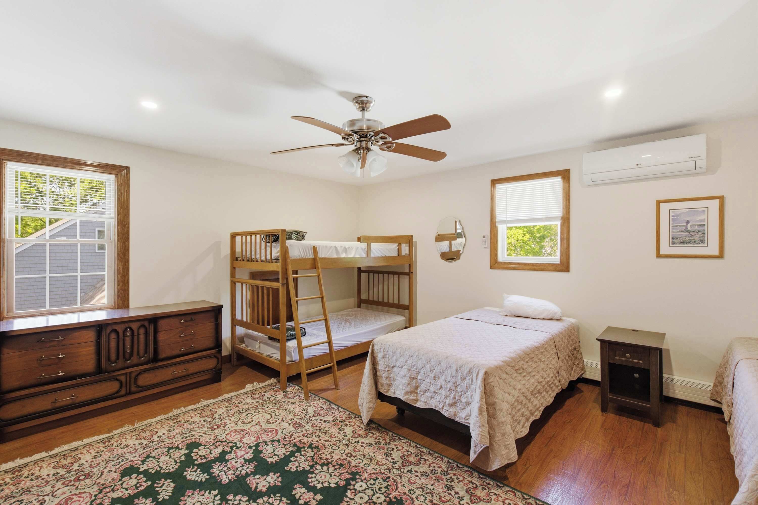 A bedroom with bunk beds, a ceiling fan, an air conditioning unit, a dresser, and a window with blinds.