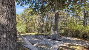 A hammock between trees, a picnic table, and a small table in a wooded area.