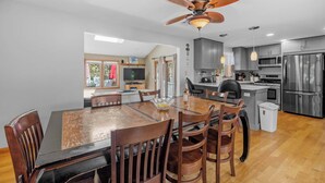 A modern kitchen with stainless steel appliances, a dining area with a wooden table and chairs, and a ceiling fan.