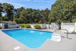 A rectangular swimming pool with a white deck, surrounded by a white fence and trees. - Bright & Spacious Poolside Cape Getaway (Mashpee)