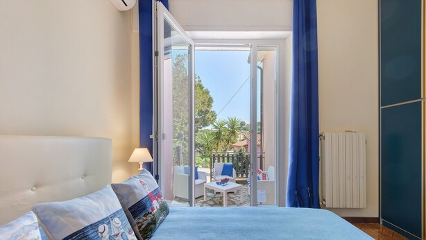 A bedroom with a bed, a nightstand, a lamp, and a view of an outdoor balcony.