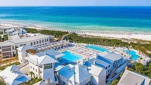 Ett semesterkomplex med flera byggnader, en stor pool och utsikt över stranden.
