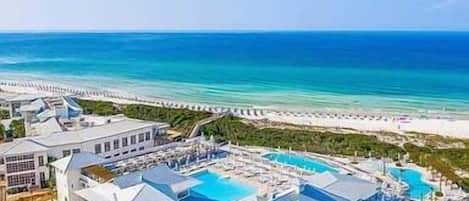 A resort with multiple buildings, a large swimming pool, and a beach view.