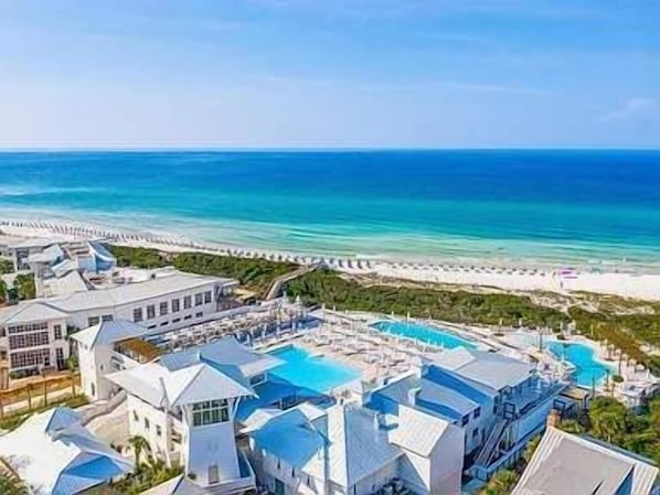A resort with multiple buildings, a large swimming pool, and a beach view.
